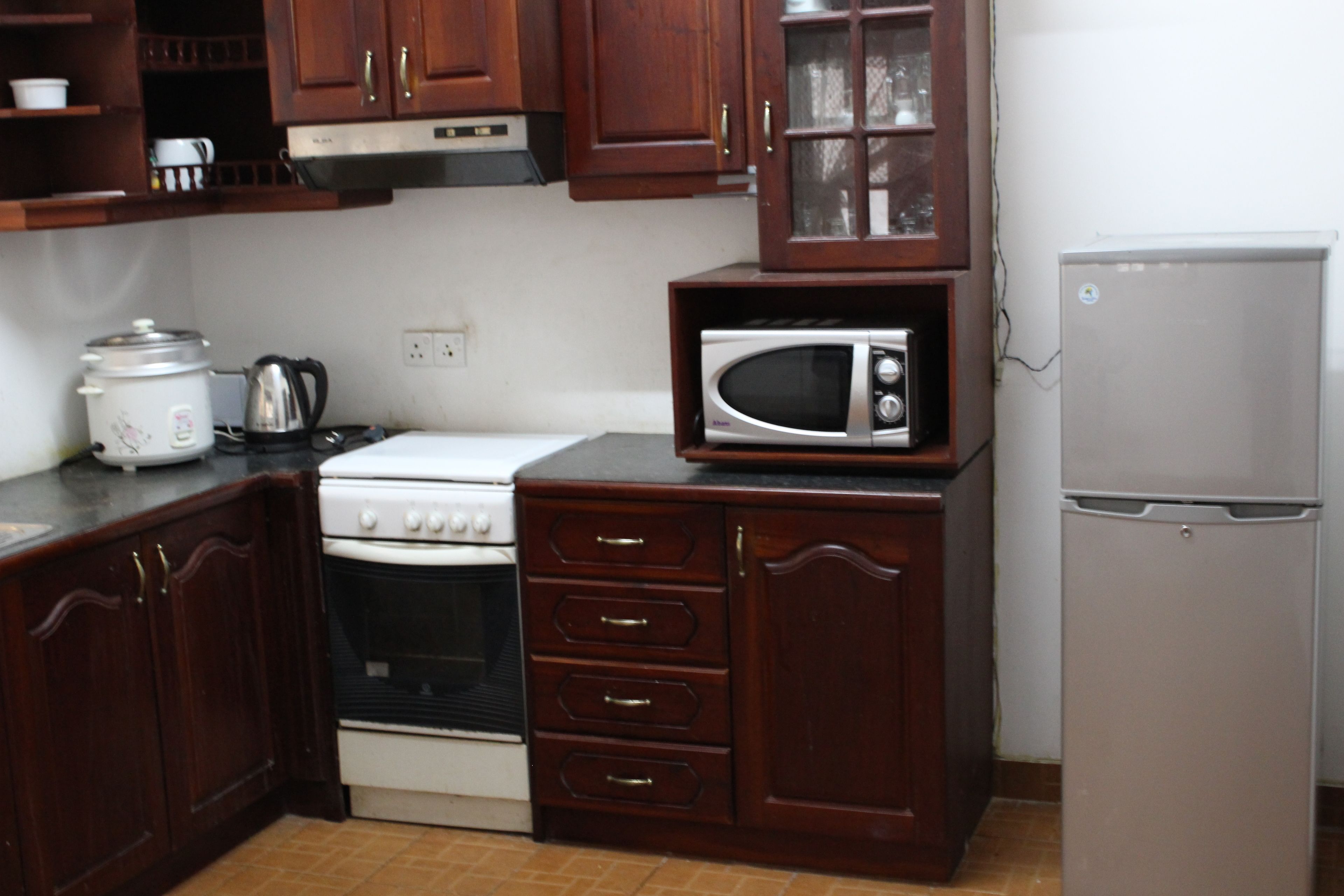 A compact kitchen with wooden cabinets, a stove, a microwave, and a refrigerator.