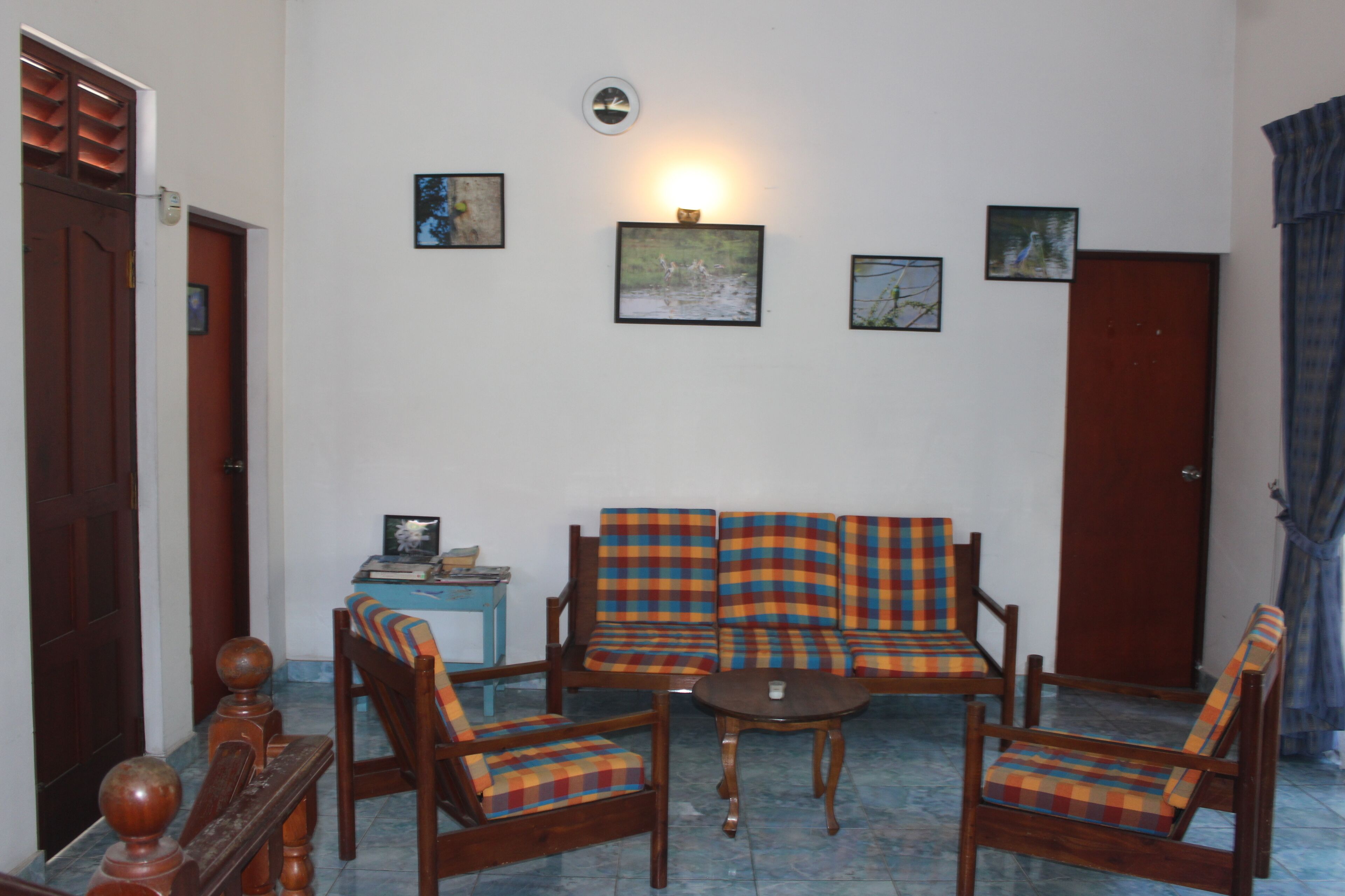 A living room with a sofa, two armchairs, a coffee table, and a side table. There are framed pictures on the wall and a door in the background.