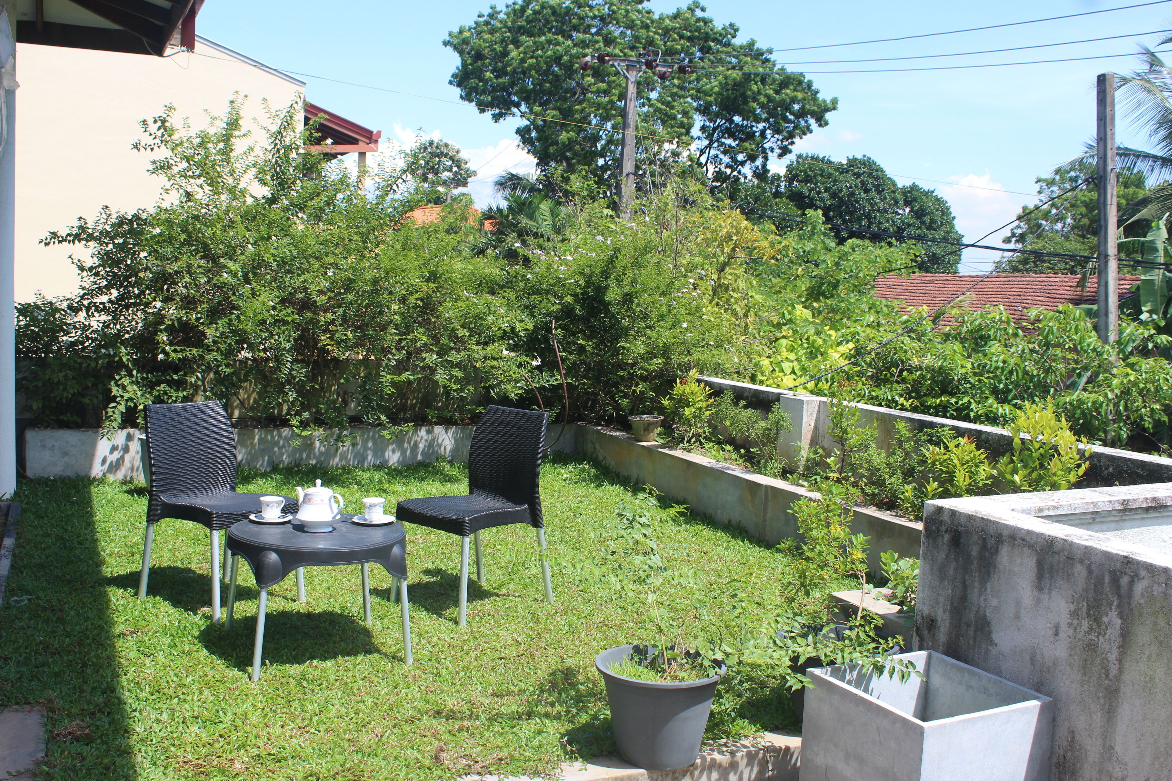 A patio with two chairs and a table, surrounded by greenery and a concrete wall.