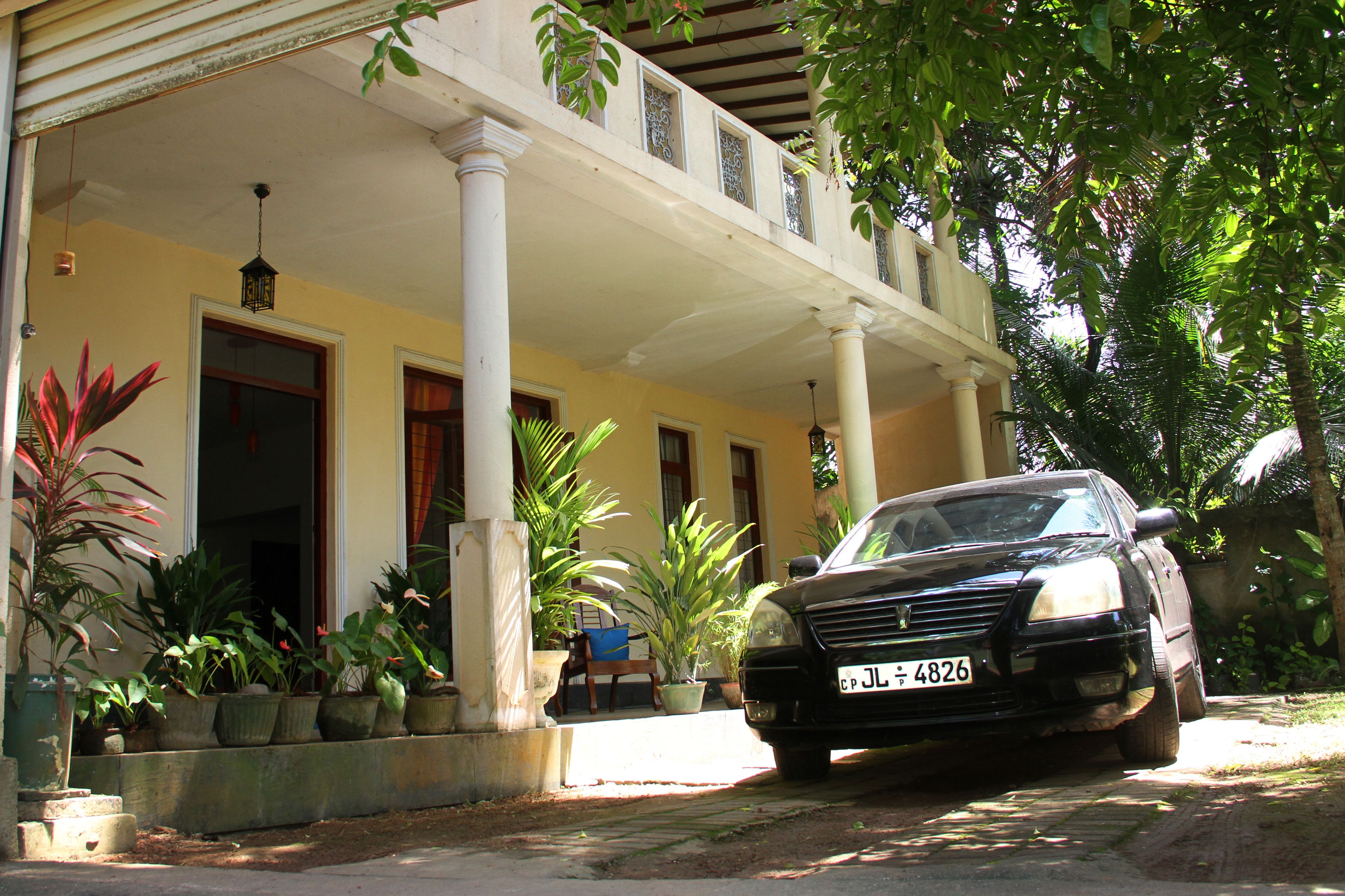 A car parked in front of a building with a covered porch, columns, and potted plants.