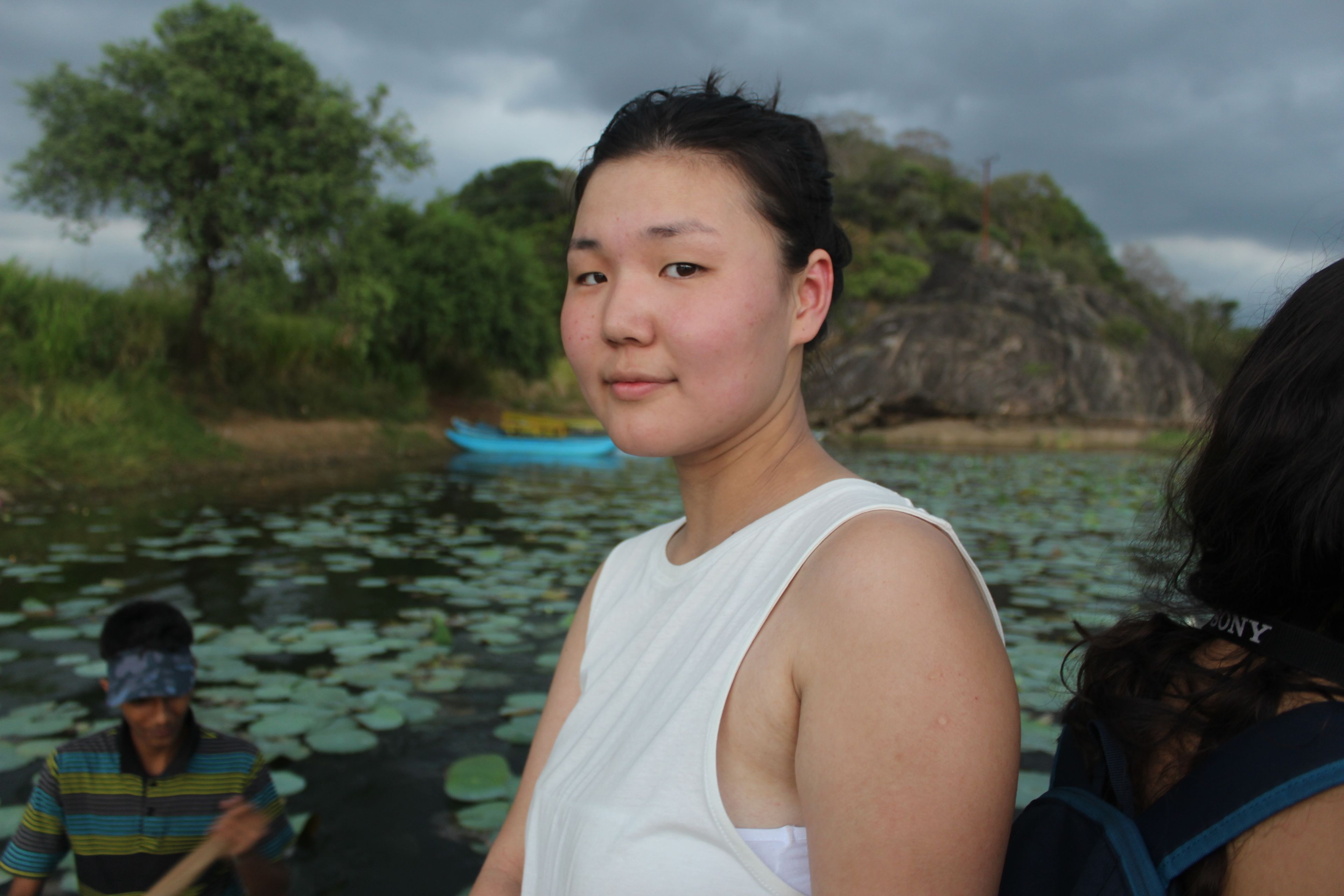 A person standing by a body of water with lily pads, trees, and a rocky outcrop in the background.