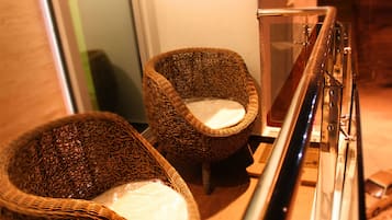 Dos sillas de mimbre con cojines blancos, ubicadas cerca de una barandilla de cristal en un espacio interior bien iluminado.