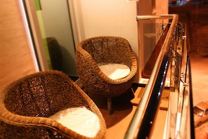 Deux fauteuils en osier avec des coussins blancs, placés près d’une rambarde en verre dans un espace intérieur bien éclairé.