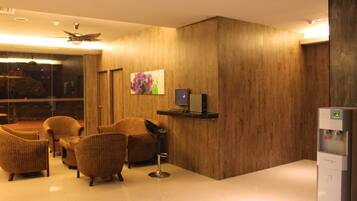 A hotel lobby with a wooden wall, a ceiling fan, a TV, and a water dispenser.