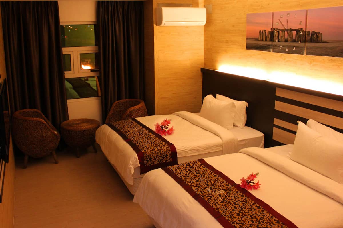 A hotel room with two beds, a small seating area, and a window with curtains.