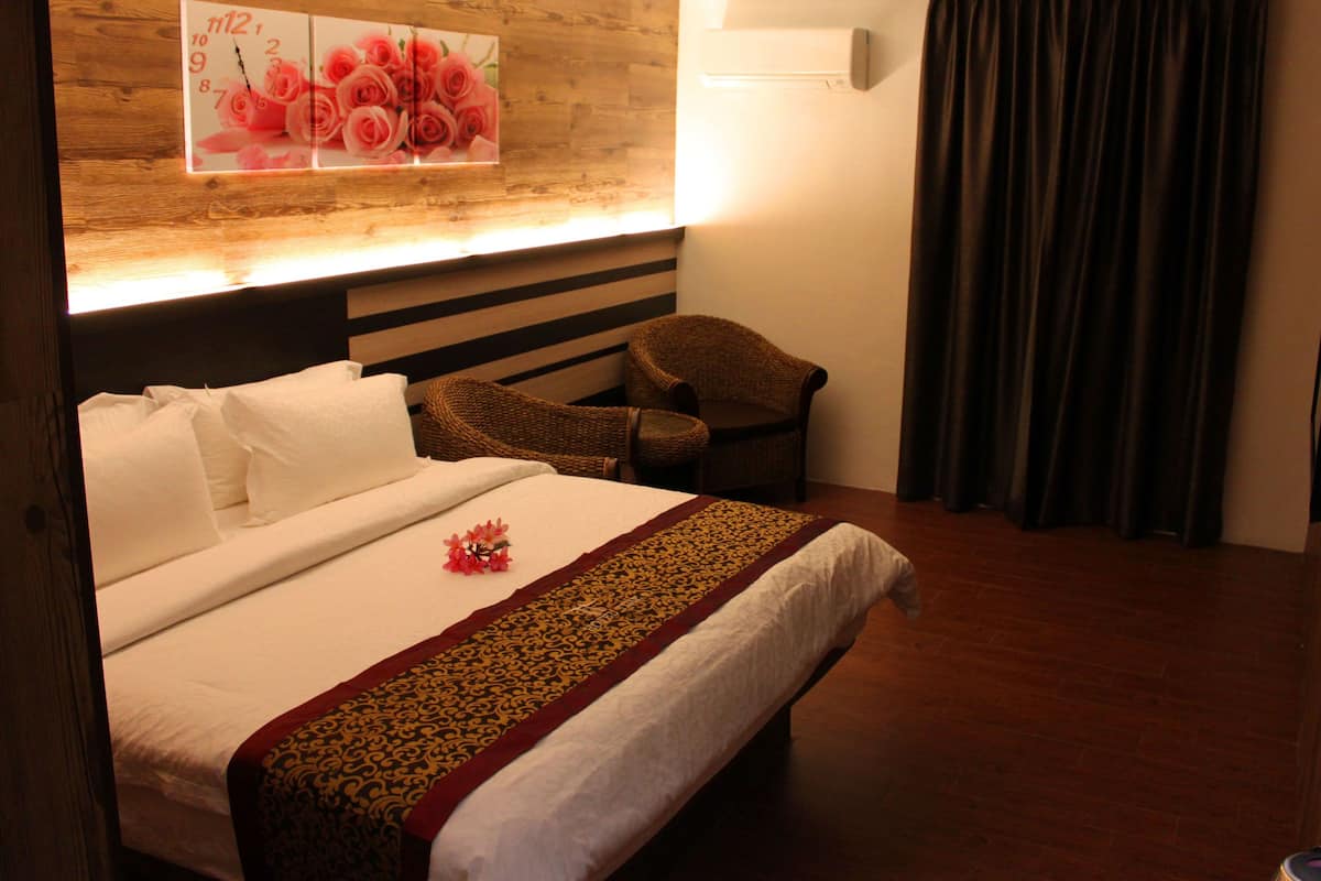 A hotel room with a bed, a chair, a wall clock, and a window with curtains.