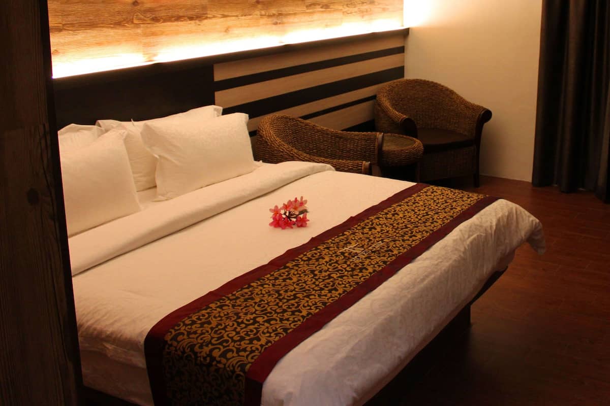 A hotel room with a bed, a chair, a wooden headboard, a window with curtains, and a wooden floor.
