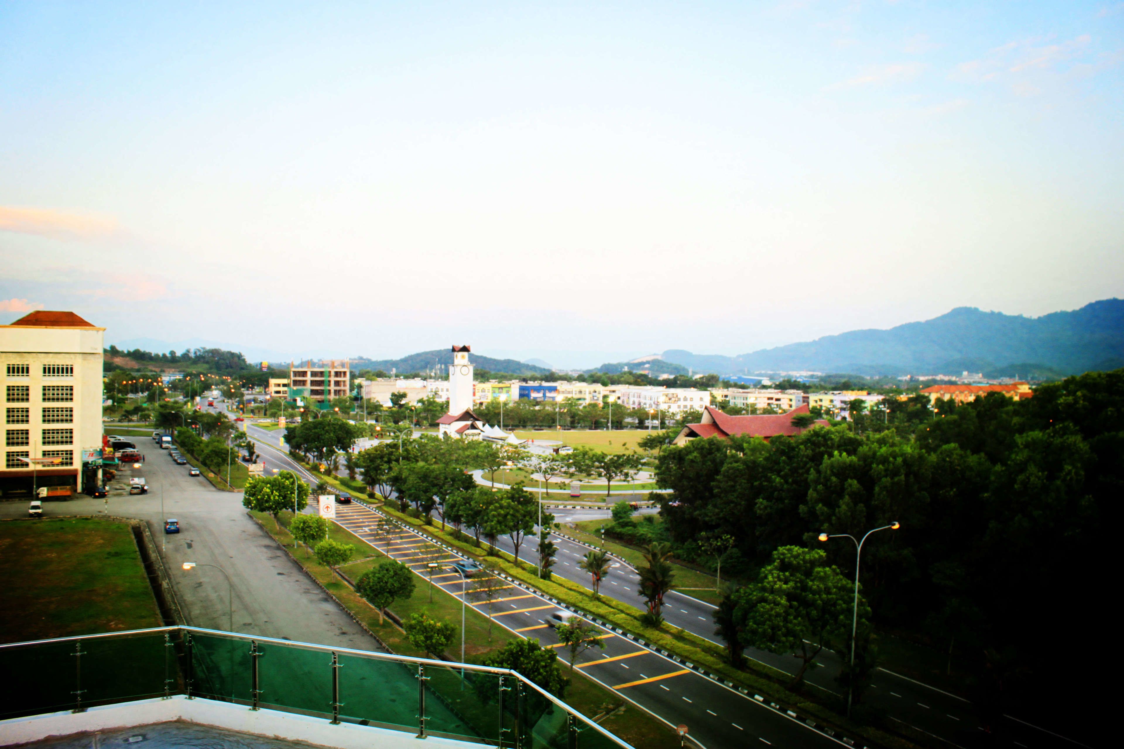 A cityscape with a prominent clock tower, a large parking lot, and a view of distant mountains.