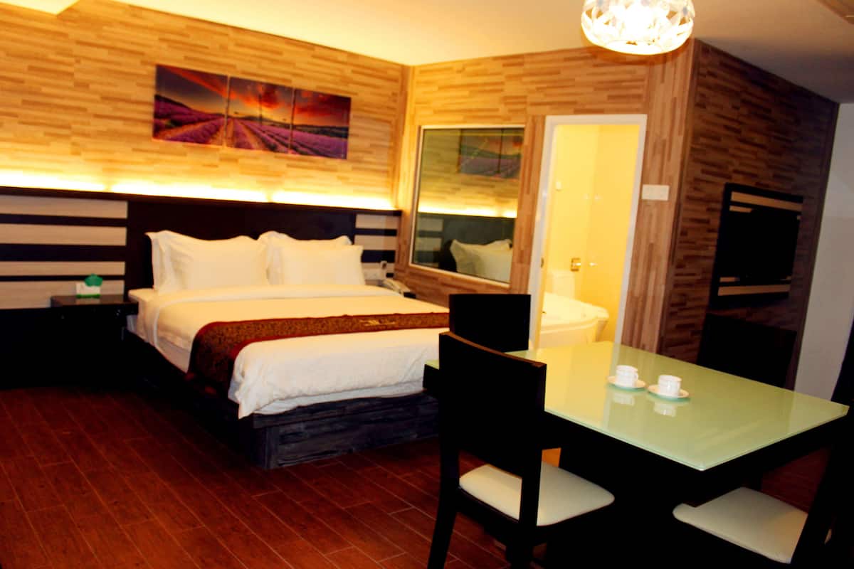 A hotel room with a bed, bedside table, nightstand, and a dining area with a table and chairs.