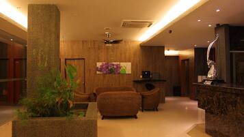 A lobby with a reception desk, seating area, and a large pillar with plants.