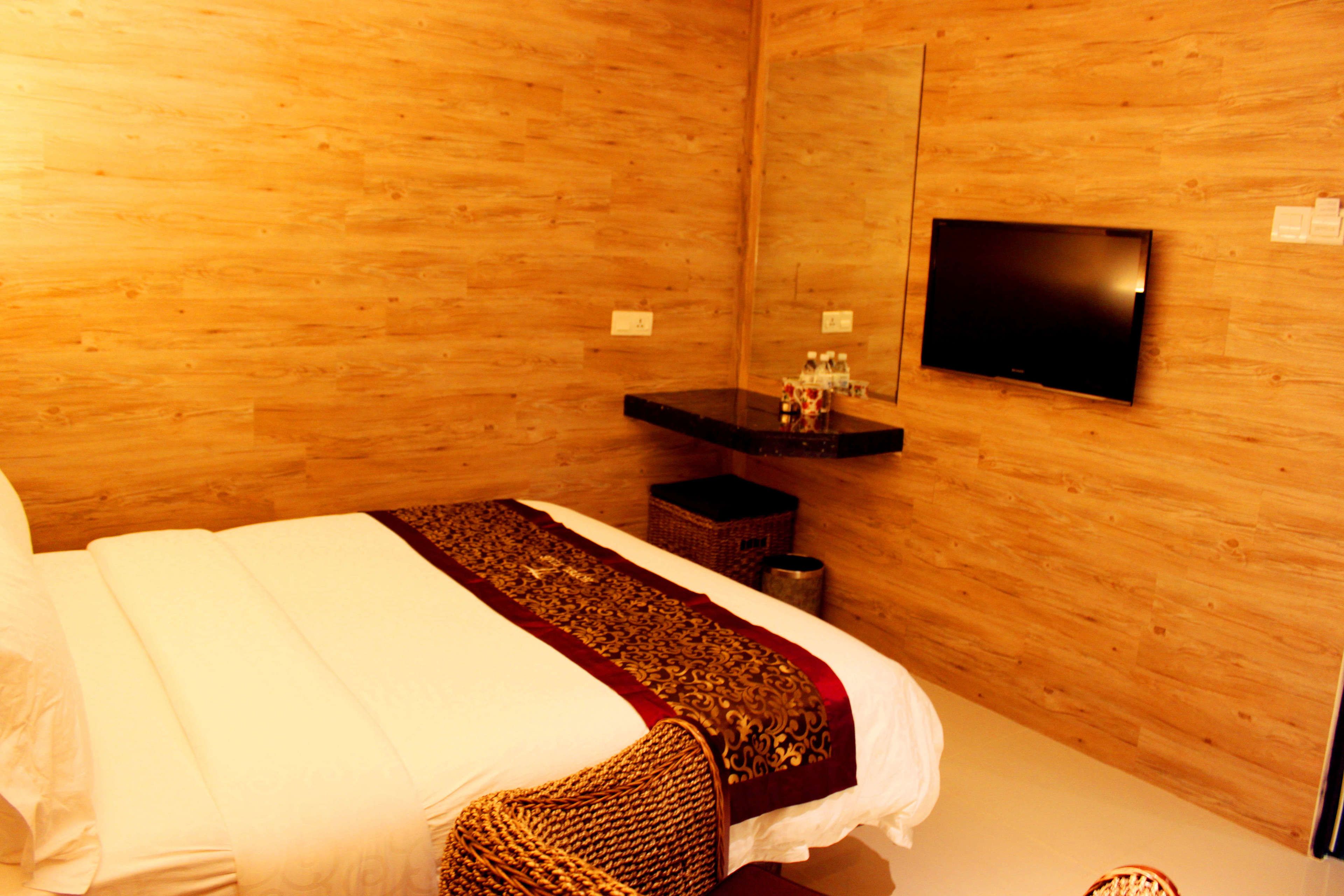 Una habitación con paneles de madera, una cama, un televisor de pantalla plana montado en la pared y un pequeño estante con artículos de tocador.
