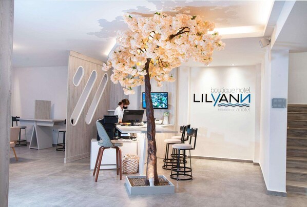 Zona de recepción de un hotel boutique con diseño moderno, que incluye un mostrador de recepción, un área de estar y un gran árbol decorativo con flores.