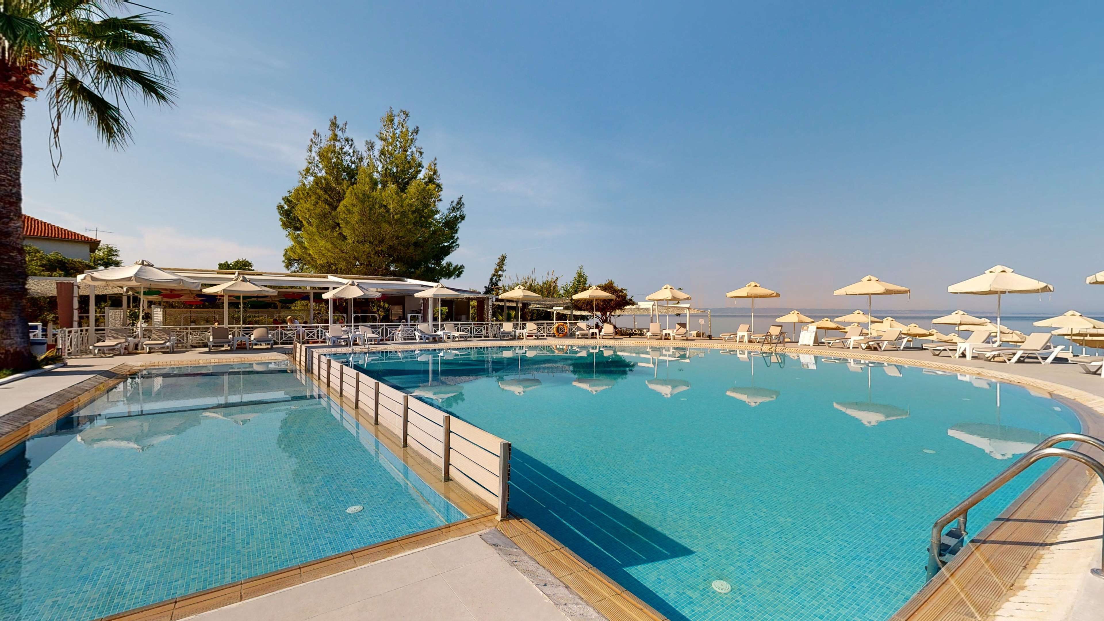 Ein Pool mit Liegestühlen und Sonnenschirmen, umgeben von Bäumen und einem Gebäude mit Außenbereich.