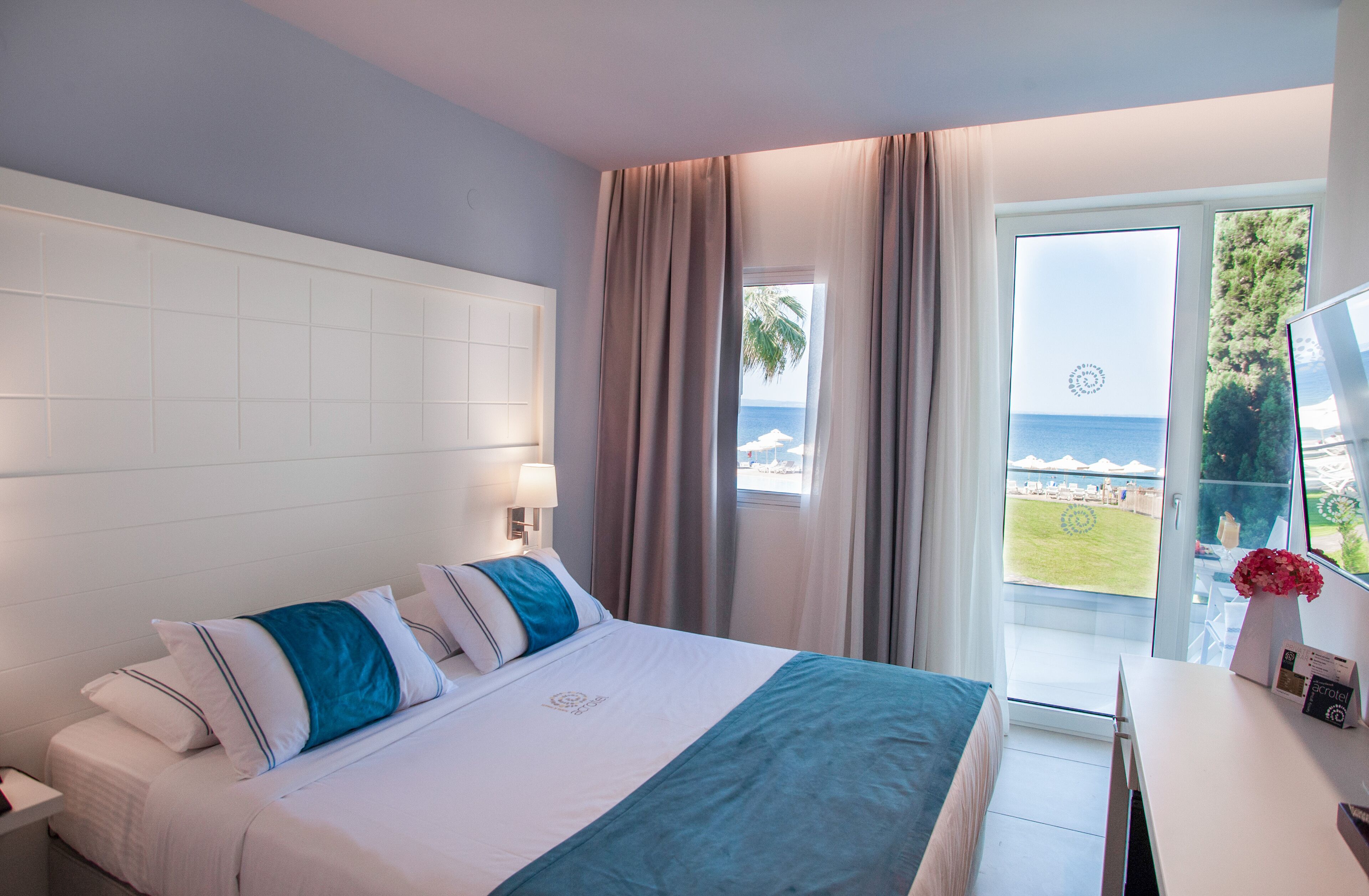 A hotel room with a bed, a desk, and a view of the sea through a large window.