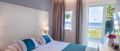 A hotel room with a bed, a desk, and a view of the sea through a large window.