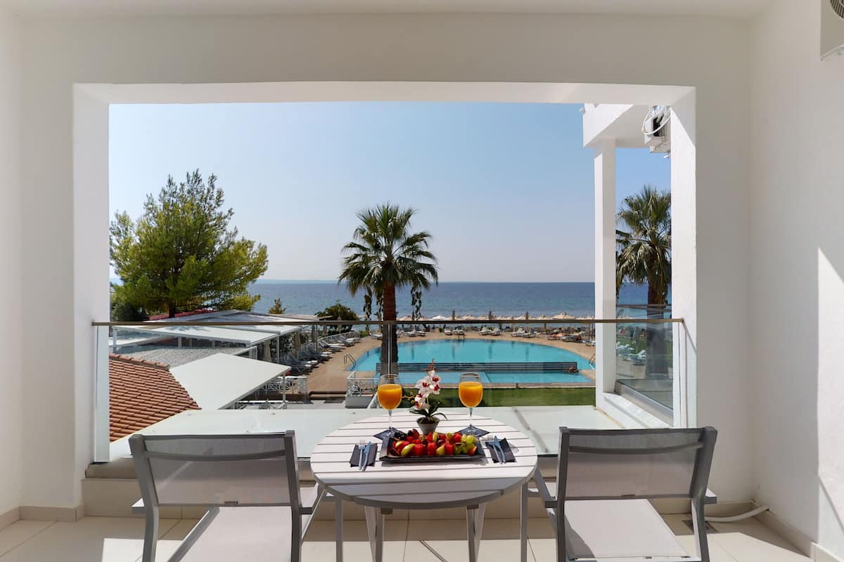 Ein Balkon mit Tisch für zwei Personen, mit Blick auf Pool und Strand.