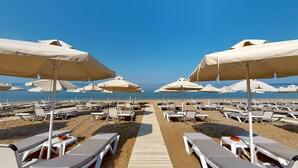 Een strand met rijen ligbedden en beige parasols.