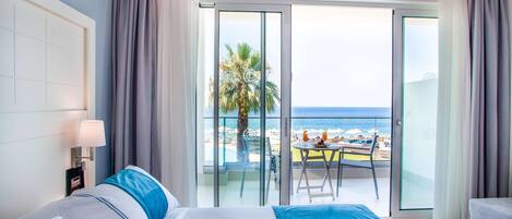 Een hotelkamer met een groot bed, een nachtkastje, een lamp en uitzicht op het strand door een glazen schuifdeur.