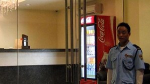 Un hombre con uniforme de pie en un vestíbulo con un refrigerador de Coca-Cola y un mostrador de recepción.