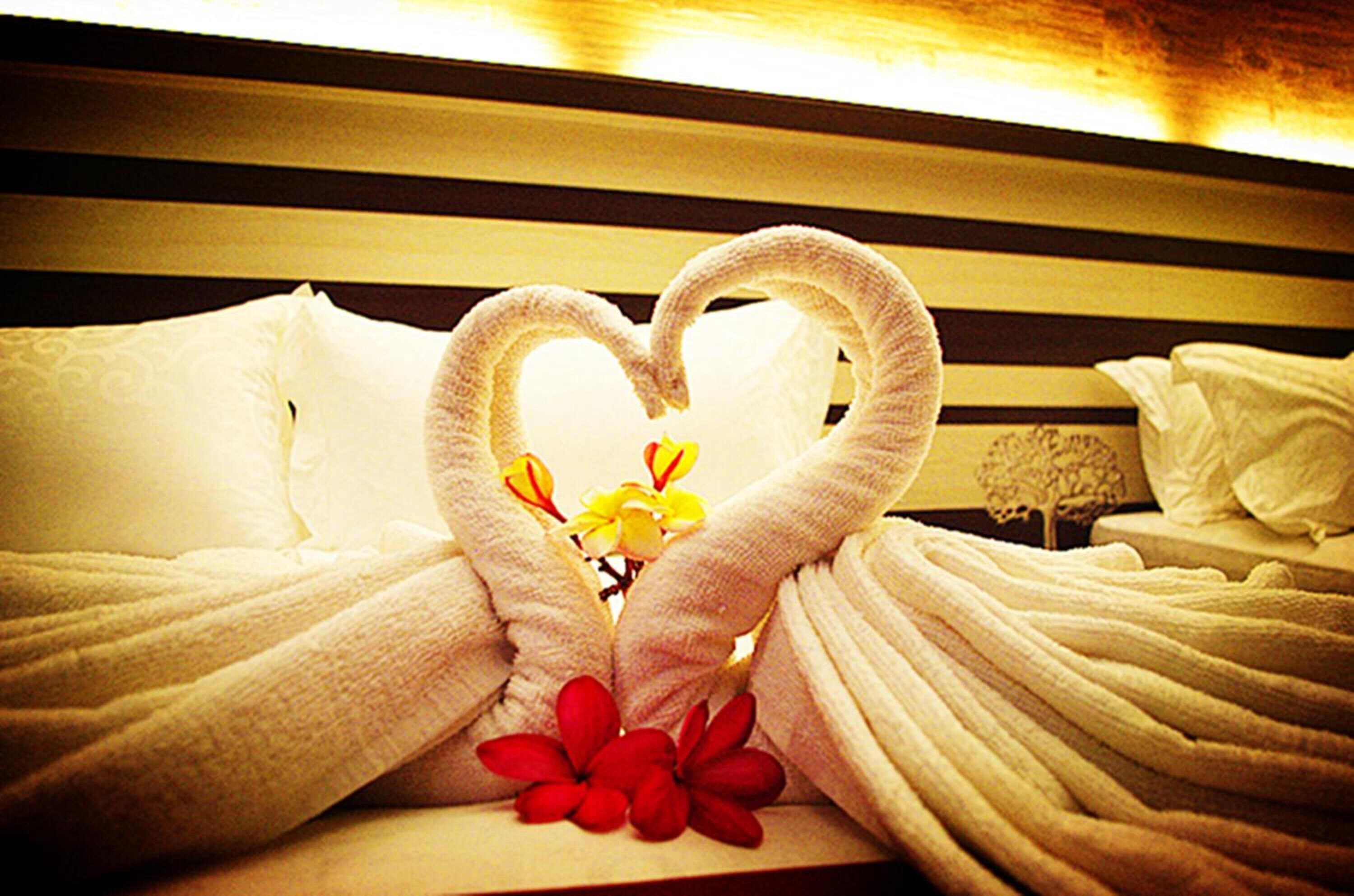 A bed with white linens and a heart-shaped towel arrangement.