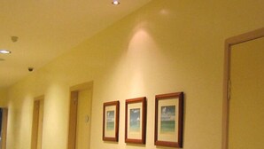 Un pasillo con tres cuadros en la pared, una puerta a la derecha e iluminación empotrada en el techo.