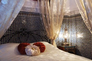 Quarto com parede estampada, cama com almofadas e mesa de cabeceira com abajur.
