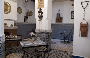Quarto com tema marroquino, piso de azulejos estampados, mesa de jantar com cadeiras, relógio decorativo na parede e diversos objetos fixados na parede.
