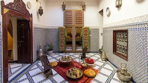 Um interior tradicional marroquino com soalho em azulejos, mobiliário de madeira ornamentado e uma porta decorativa.