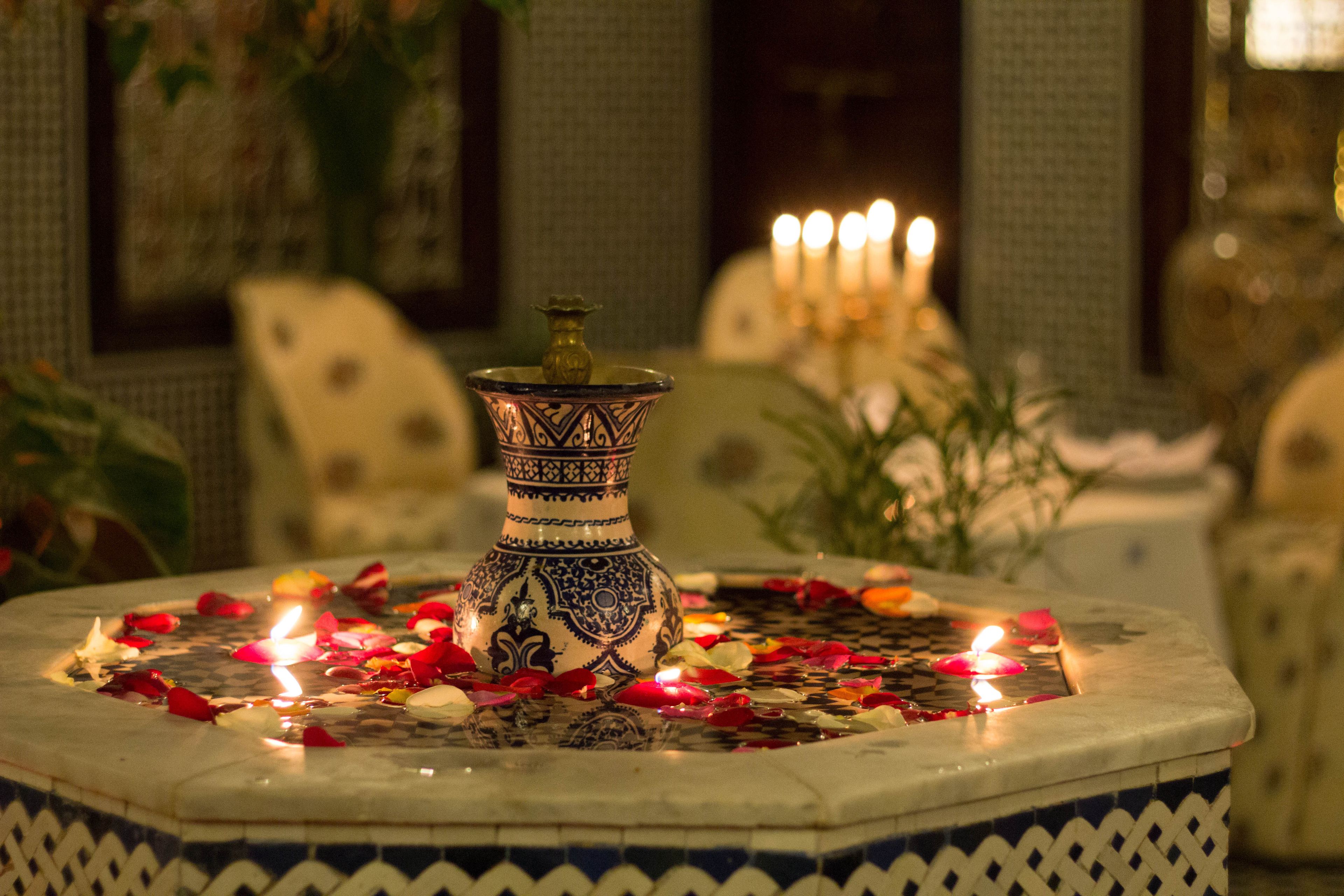 A decorative fountain with a patterned vase, surrounded by rose petals and candles.