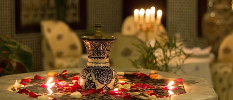 A decorative fountain with a patterned vase, surrounded by rose petals and candles.