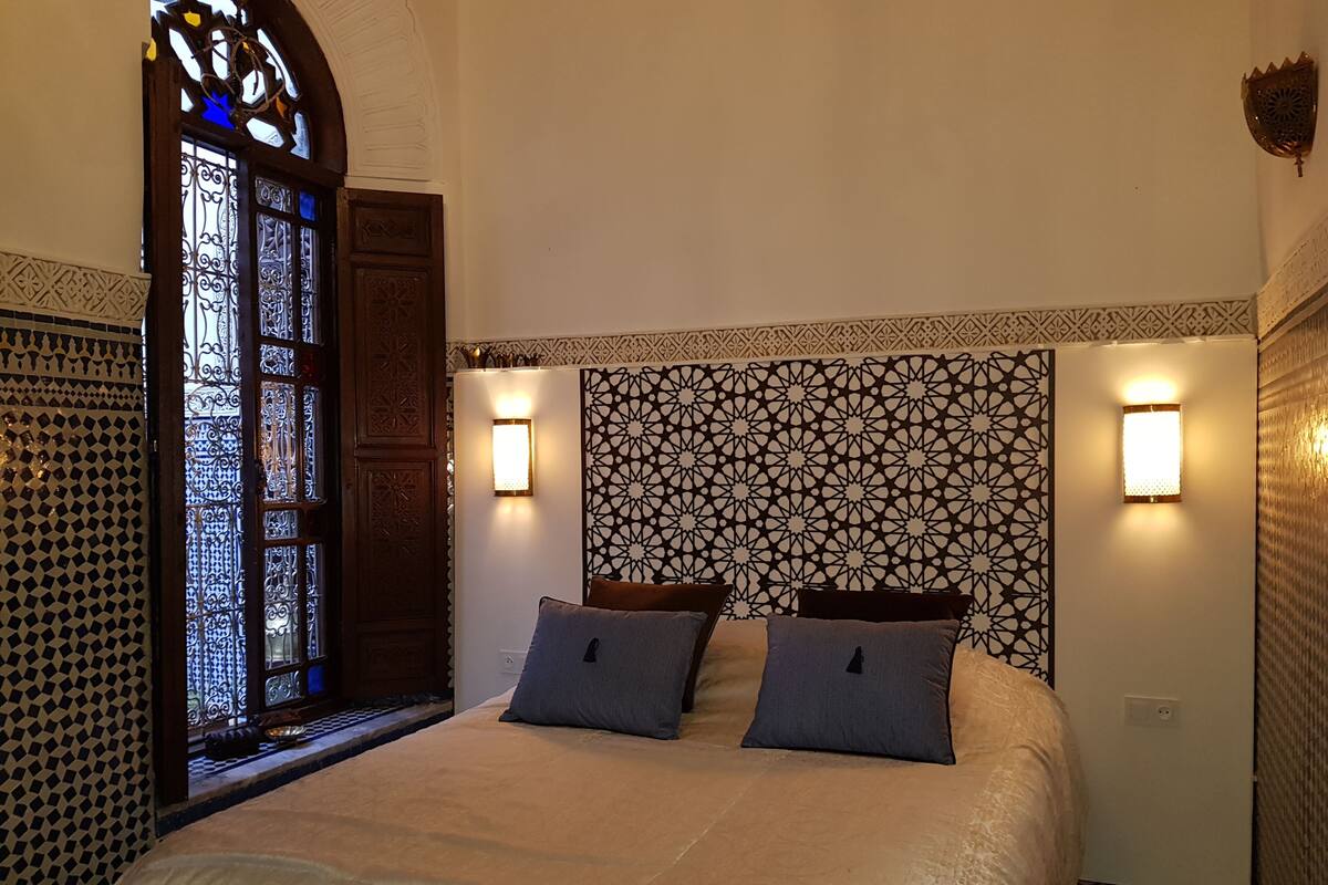 A bedroom with a large bed, two wall-mounted lights, a decorative door, and patterned walls.
