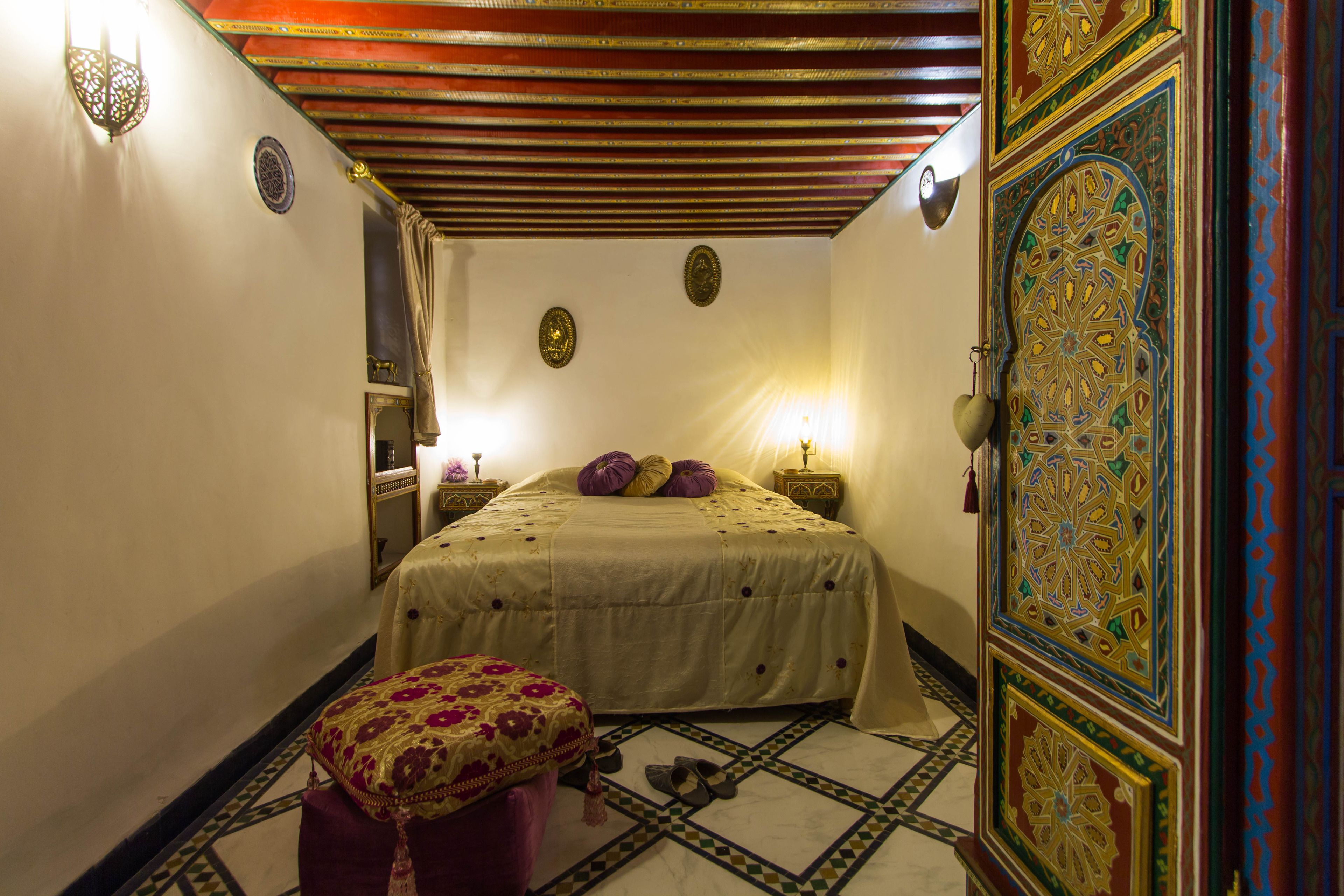 A room with a bed, a nightstand, a wall-mounted lamp, and a decorative door.