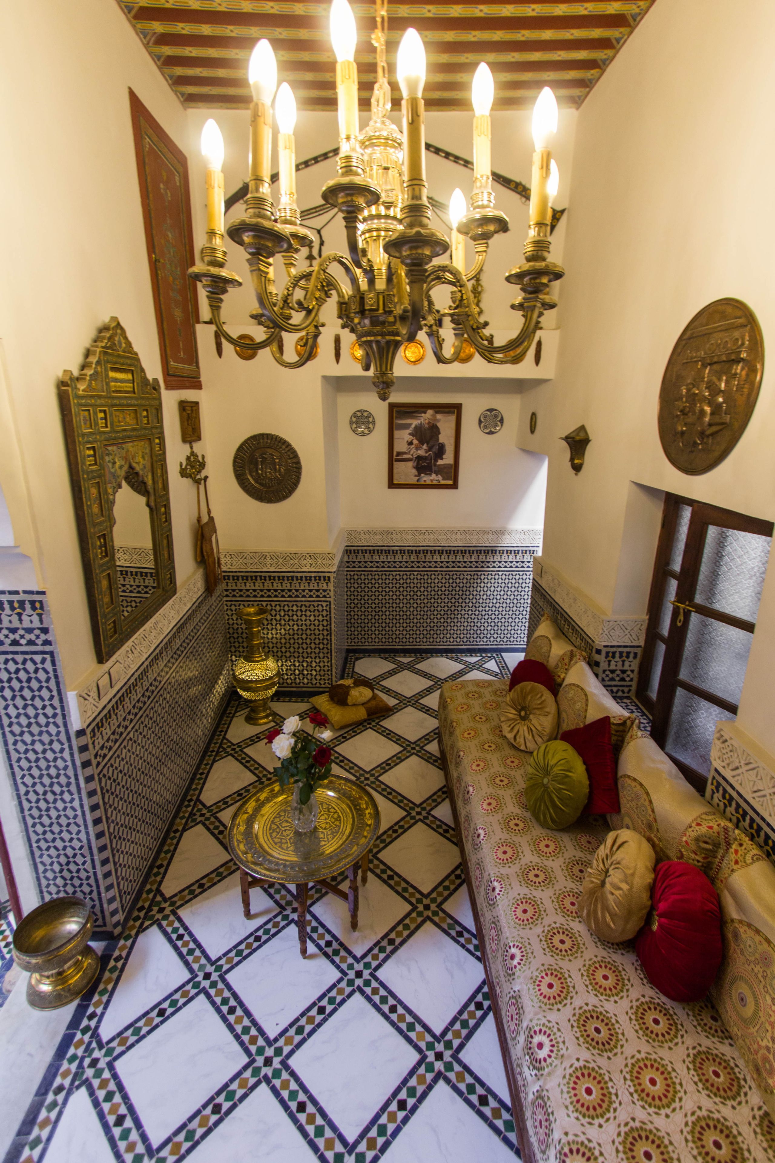 Un intérieur marocain traditionnel avec un sol à motifs, un canapé agrémenté de coussins, une lampe en laiton et un lustre.