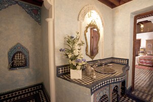 Um banheiro com piso quadriculado, um espelho decorativo e um arranjo floral.