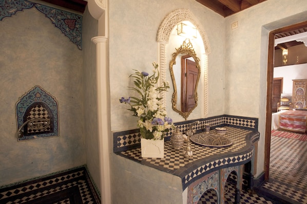 Un baño con piso a cuadros, un espejo decorativo y un arreglo floral.