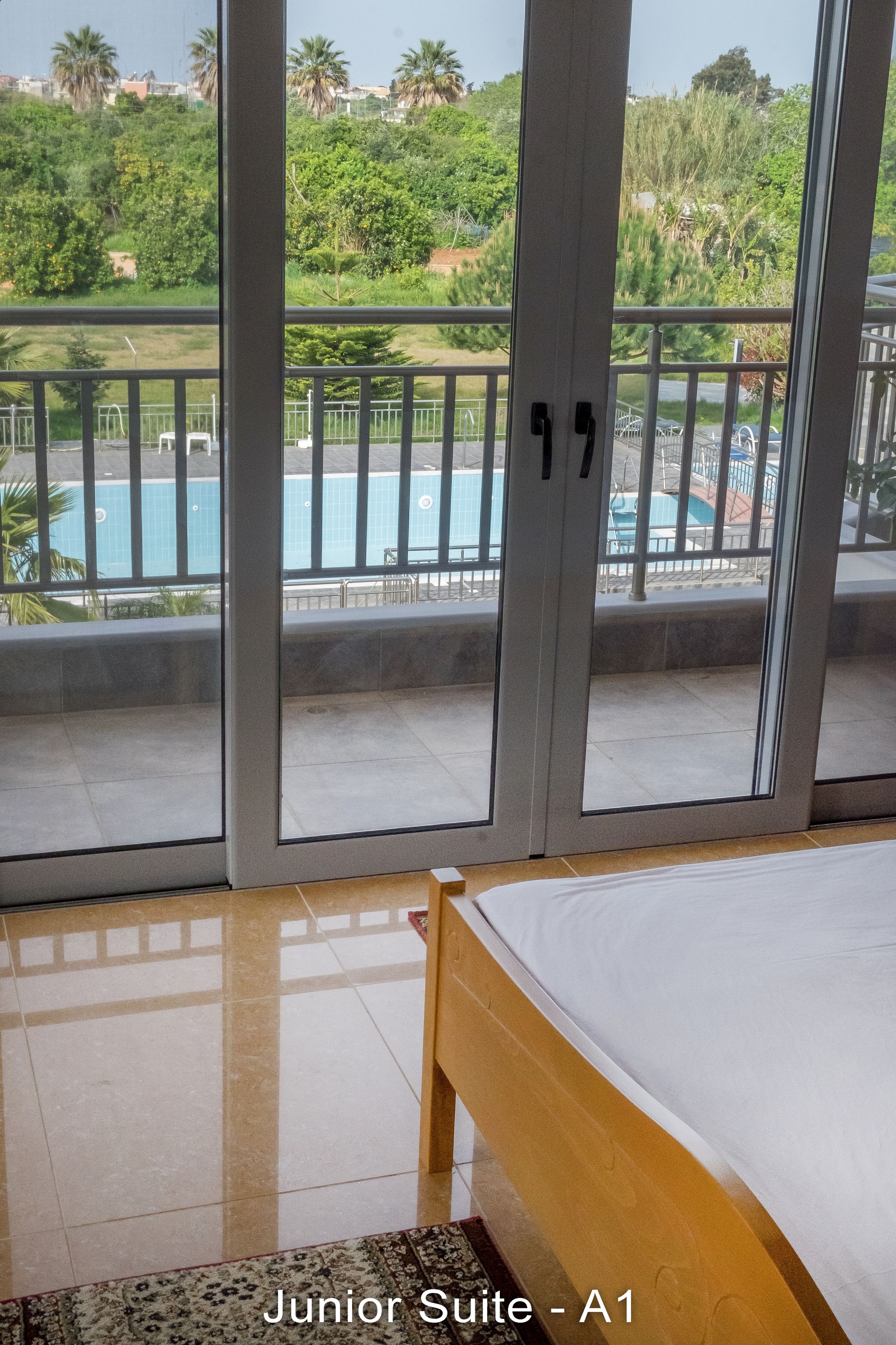 Una suite junior con cama, vista a una piscina y balcón con barandilla.