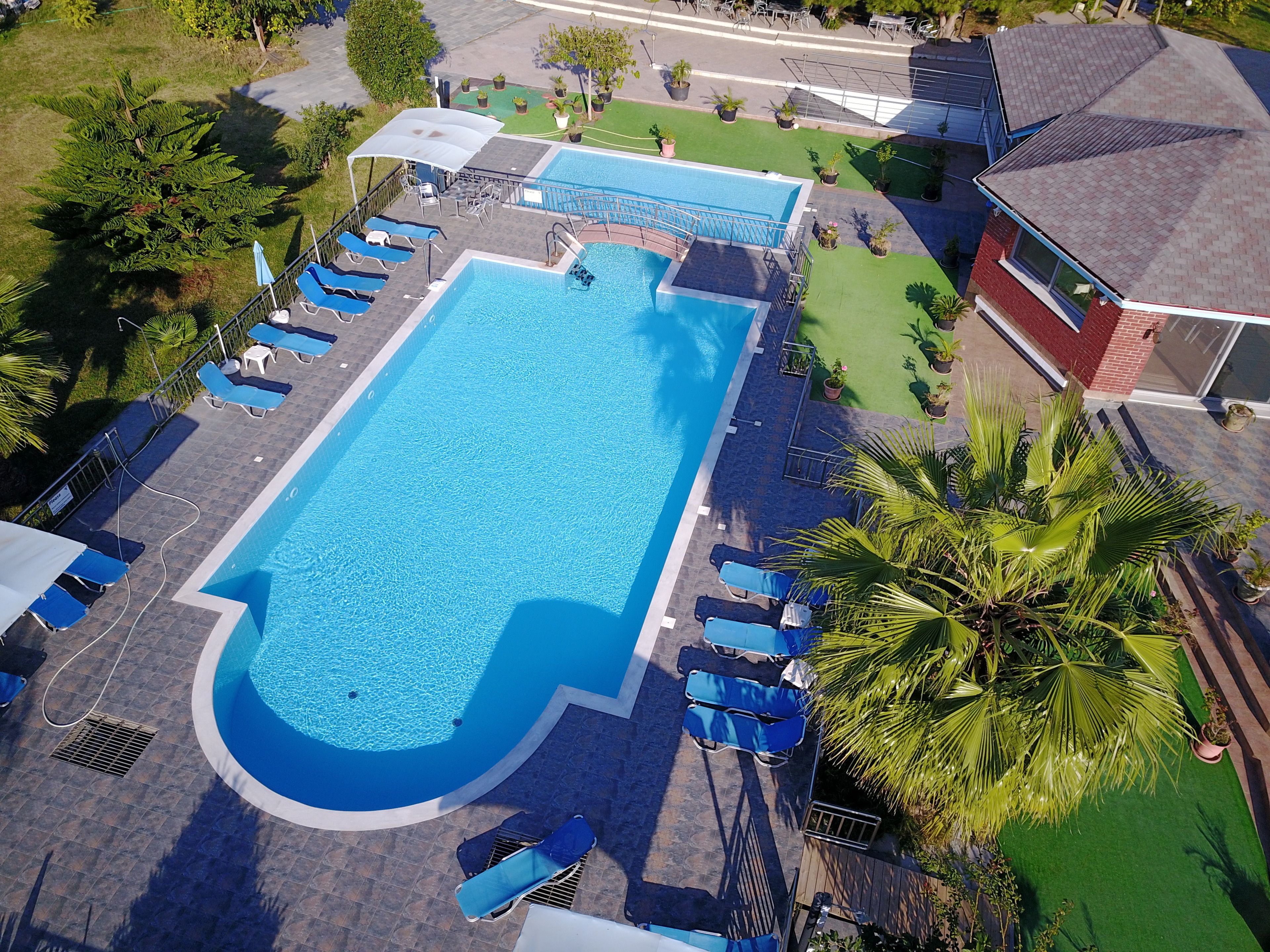 Vue aérienne d’une piscine rectangulaire entourée d’une terrasse, aménagée avec plusieurs chaises longues et un espace salon couvert.