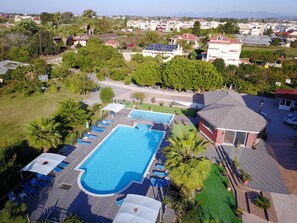 A large swimming pool with sun loungers and a covered area, surrounded by greenery and residential buildings. - IonionStar Hotel (Preveza)