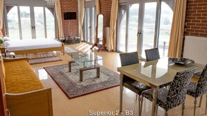Una habitación amplia con cama, una mesa de comedor de cristal, sillas estampadas y vistas amplias por puertas correderas.