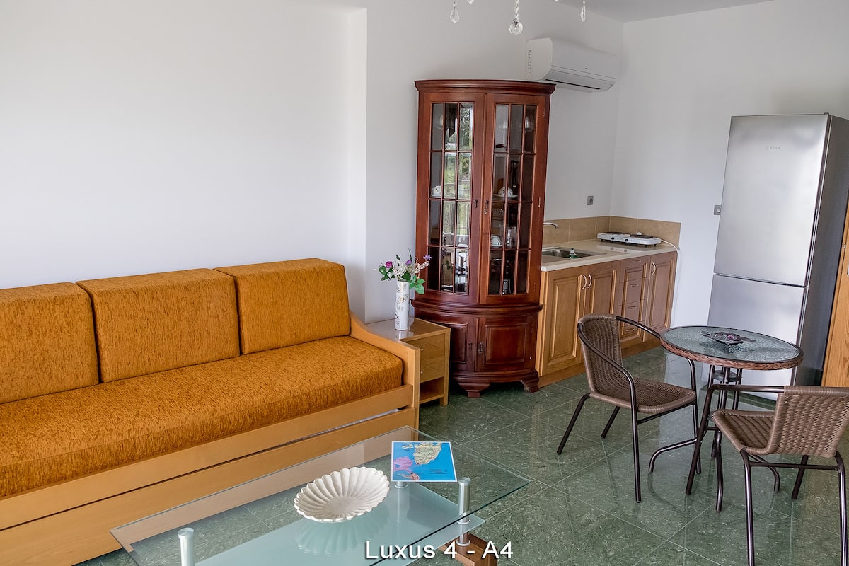 A compact living space with a sofa, dining table, chairs, a cabinet, and a refrigerator.
