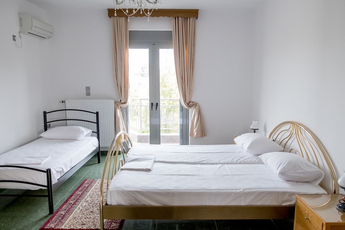 A room with two single beds, a radiator, a wooden nightstand, and a window with curtains.