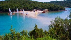 Zona costera con barcos, una playa arenosa y una colina boscosa.