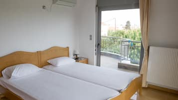Un lit double avec du linge de lit blanc, une tête de lit en bois, une table de chevet avec une lampe, et une vue sur un balcon avec une balustrade.
