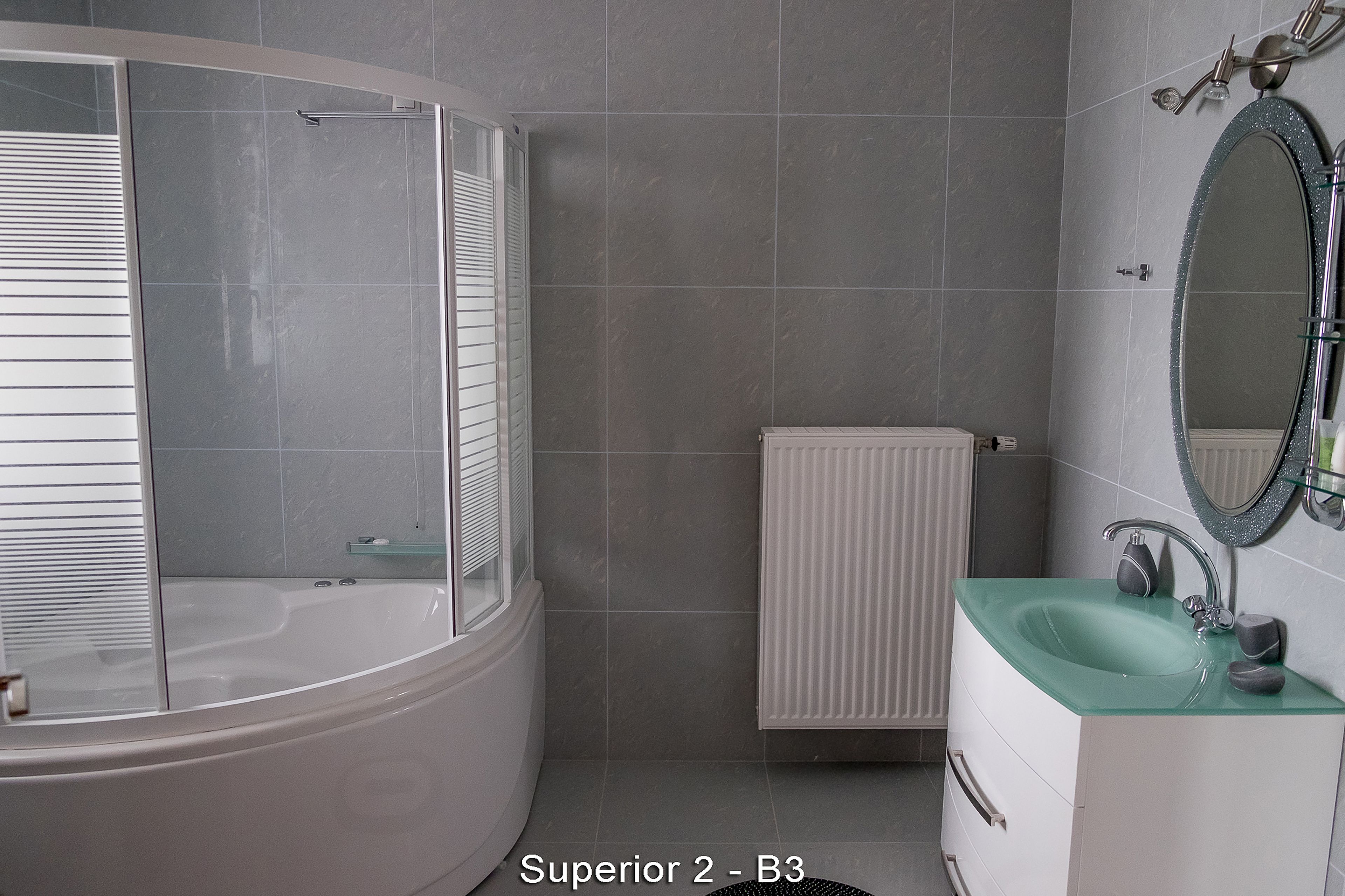 A modern bathroom with a curved bathtub, a glass shower enclosure, a white radiator, and a green sink with a mirror above it.