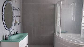 A bathroom with a glass-enclosed shower, a white bathtub, and a green sink with a mirror above it.
