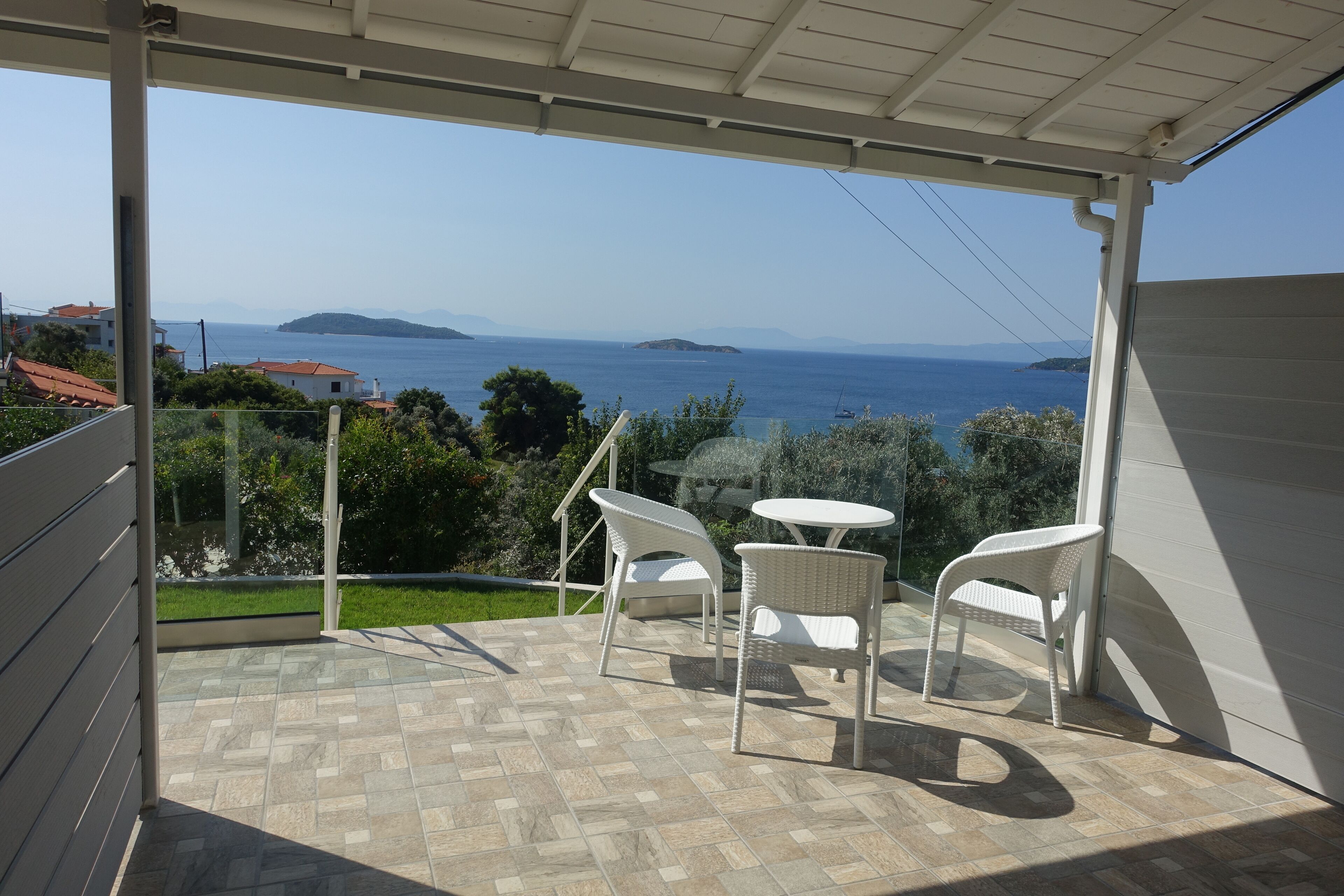 Ein Balkon mit Blick auf das Meer, zwei weiße Korbstühle und ein kleiner runder Tisch.