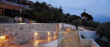 A modern outdoor patio area with stone walls, glass railings, and ambient lighting.