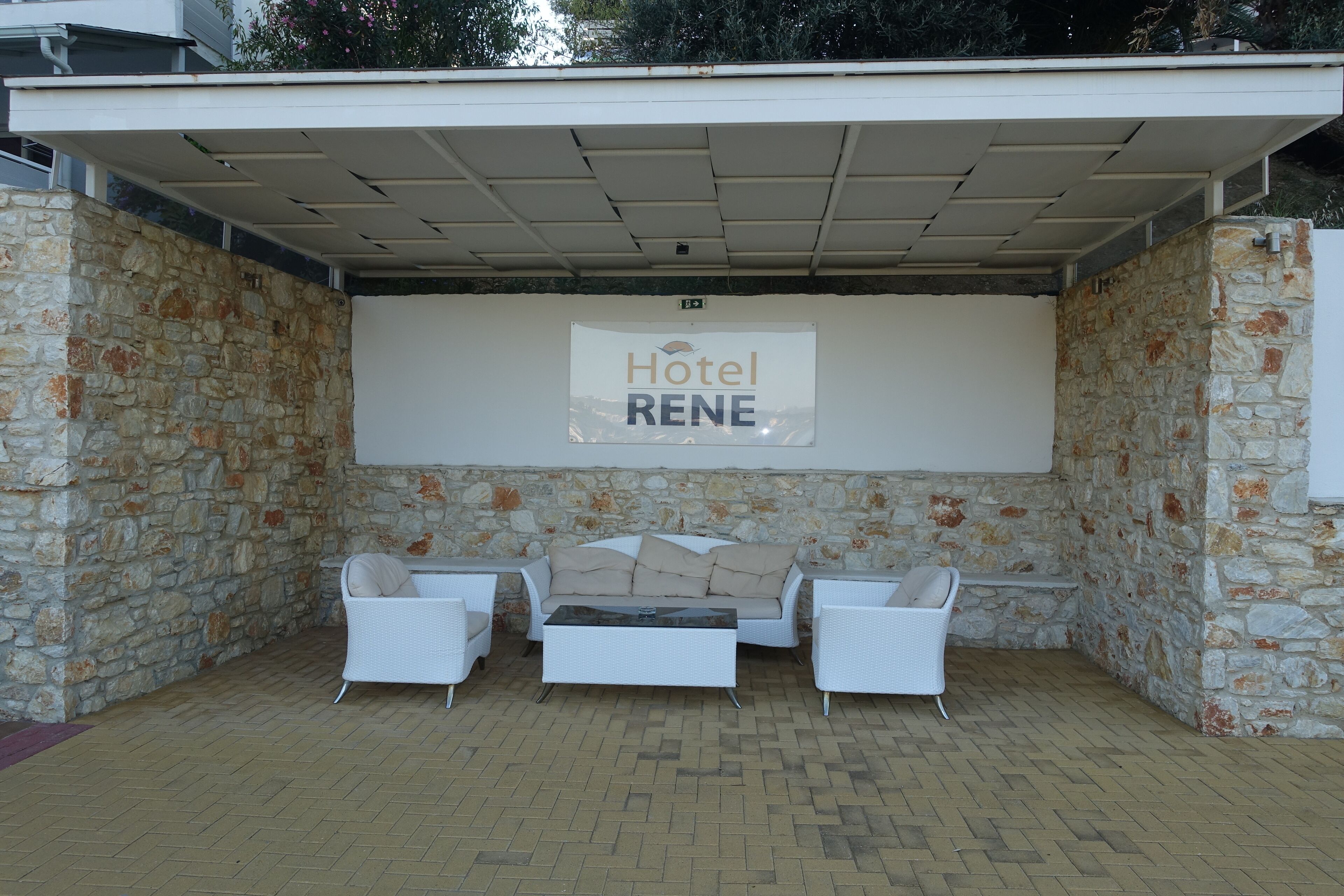 A covered outdoor seating area with stone walls, a white sofa, and a sign reading "Hotel RENE".