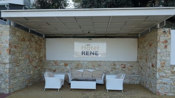 A covered outdoor seating area with stone walls, a white sofa, and a sign reading "Hotel RENE".