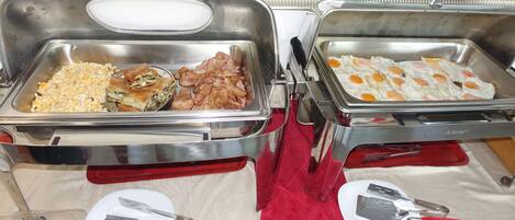 A buffet setup with various food options including eggs, bacon, and a dish with vegetables.